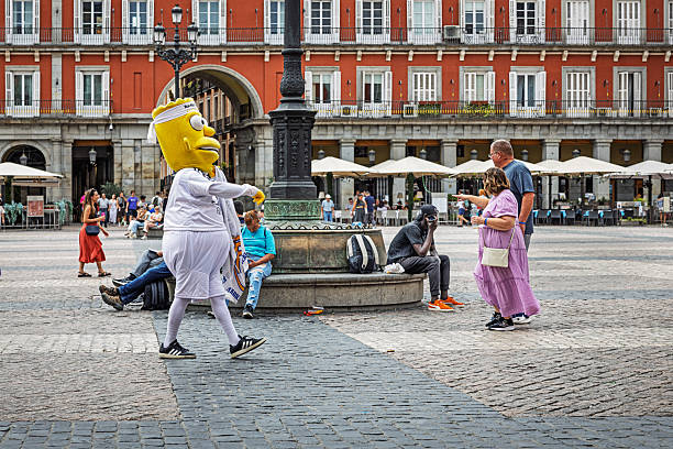 Plaza Mayor, Madrid, Spain, Europe, September 8, 2025:  A person dressed in a cartoon-inspired costume walks through Plaza Mayor in Madrid, Spain, as part of a street-level promotional stunt. The oversized character outfit stands out against the historic red-brick architecture and cobblestone square, where tourists and locals gather near outdoor cafés and restaurant seating. The image captures the playful intersection of commercial branding and cultural tourism in one of Europe’s most iconic urban spaces.