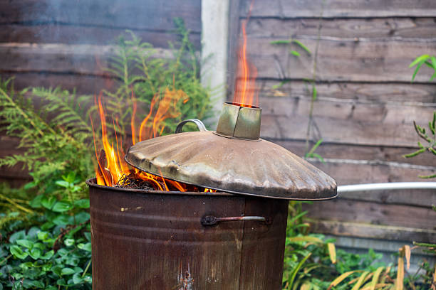 A metal bin ablaze with flames, surrounded by lush greenery.