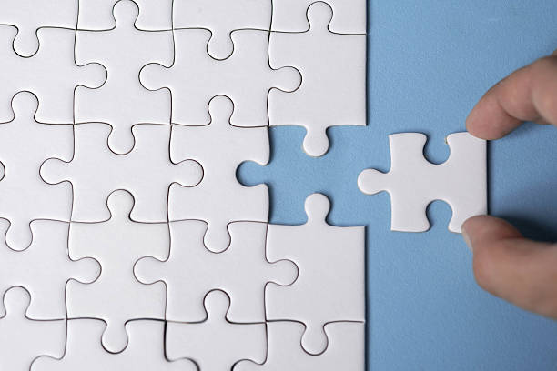 istock A hand placing the final piece into a nearly completed white jigsaw puzzle on a blue background. 2237866790