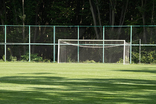 istock A large grass soccer field shows a white goal with netting. Dense trees border the area, providing shade and creating a natural setting in broad daylight 2237871232