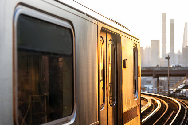This is a photograph of a subway train arriving at sunset on elevated tracks in Queens, NY on a summer day.