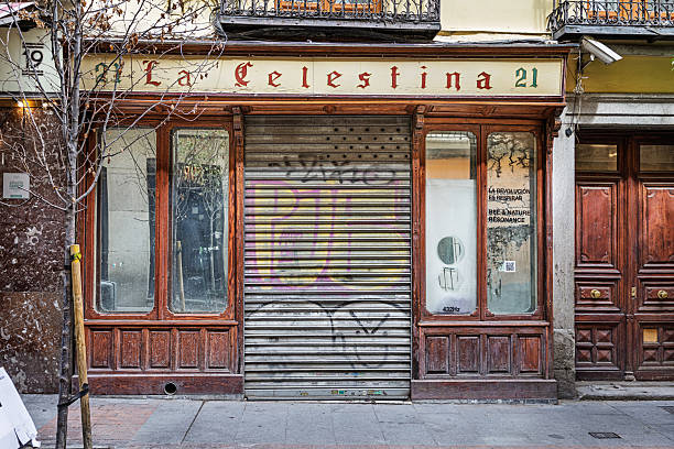 Madrid, Spain, Europe, September 8, 2025:  The shuttered entrance of a small restaurant in Madrid, Spain, displays signs of closure and urban wear. Metal security shutters covered in graffiti conceal the storefront, while faded signage and empty windows suggest the business has ceased operations. Framed by traditional architecture and street-level details, the image reflects the economic shifts and evolving commercial landscape in one of Europe’s most vibrant capital cities.