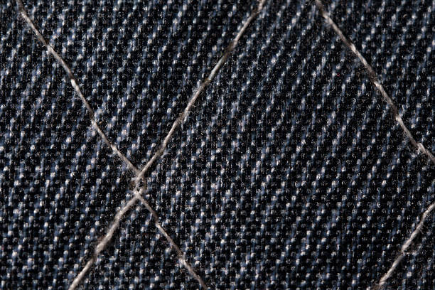 Macro shot of dark denim fabric with diagonal quilted stitching and visible fibers. Ideal for textile, fashion, and background use.