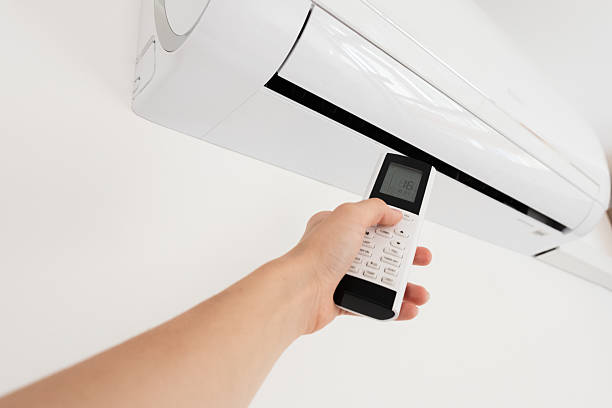 istock A hand holding a remote control aimed at a wall-mounted air conditioner. The air conditioner is white and modern in design. 2237878297