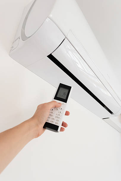 istock A hand holding a remote control aimed at a wall-mounted air conditioner. The air conditioner is white and modern in design. 2237878360