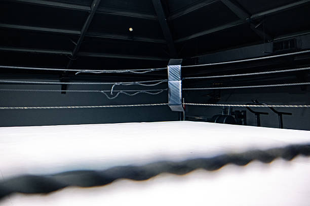 istock A boxing ring with white canvas and black ropes. The scene is dimly lit, emphasizing the structure and tension of the ring. No people are present. 2237878363