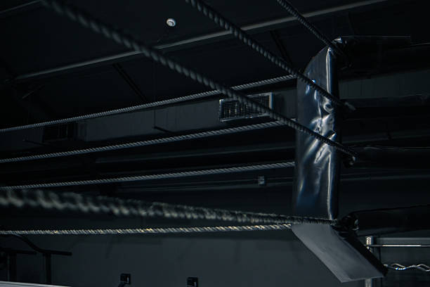 istock A boxing ring with white canvas and black ropes. The scene is dimly lit, emphasizing the structure and tension of the ring. No people are present. 2237878394