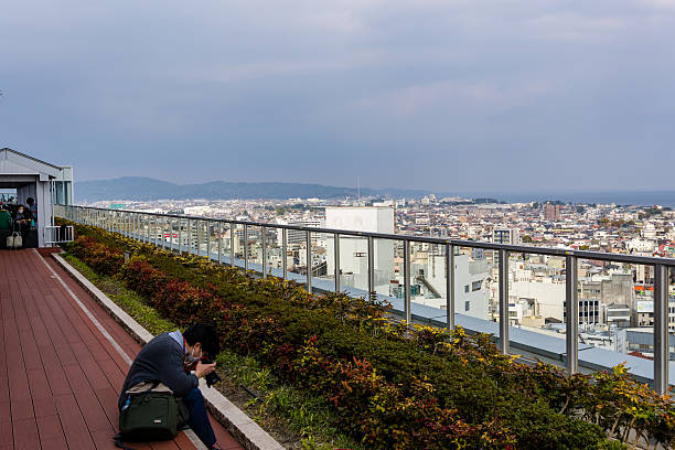 Man with camera sitting on a rooftop observation deck overlooking Odawara city, Japan.