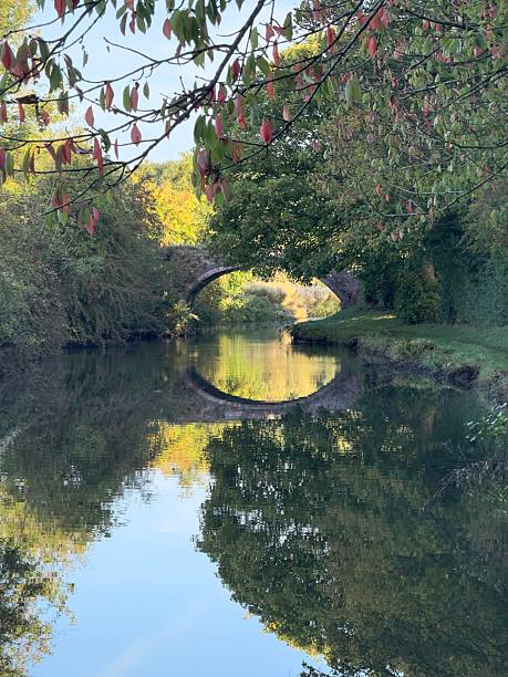 The curved arch of a canal bridge is reflected in the still waters of the Oxford Canal early in the morning