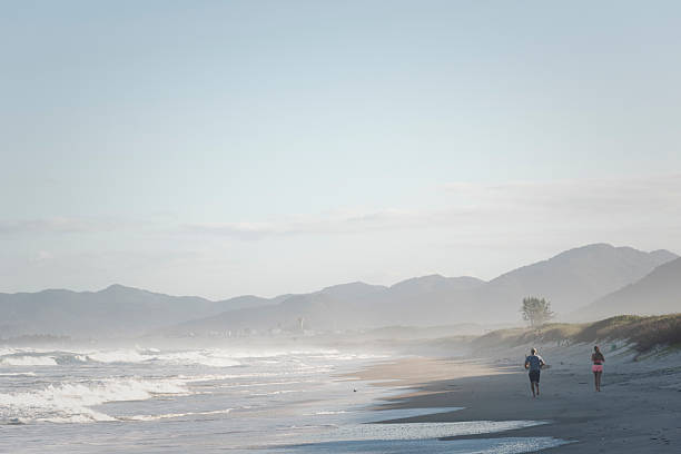 Florianopolis, Brazil - April 9, 2019: Two people jog on a pristine stretch of sand between Campeche and Joaquina beaches in Florianopolis.