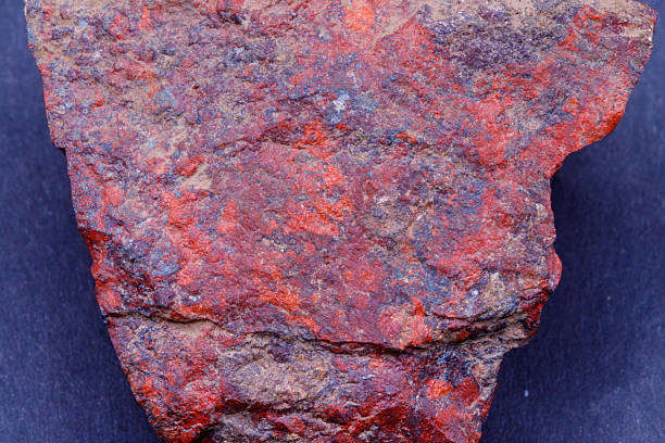 Close-up of a rough, textured mineral specimen with dominant red and dark purple hues, interspersed with lighter brown and faint blue-grey tones.