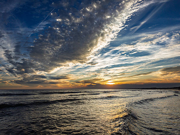 Waves gently roll in as the sun sets over the Atlantic Ocean in Huelva, Spain. Soft colors illuminate the sky and water at dusk.