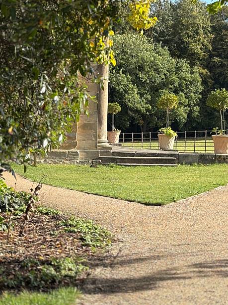 istock A tranquil garden path splits around a grassy area leading to a stone pillar structure, surrounded by potted topiary and lush trees under a clear sky, evoking peace and timeless beauty. 2237919351