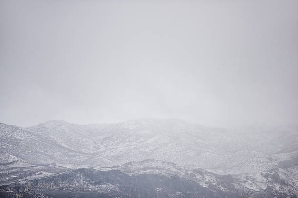 Snow-clad mountain range fading into a vast, foggy gray sky on a cold winter day, evoking a serene, desolate wilderness with soft light and ample copy space
