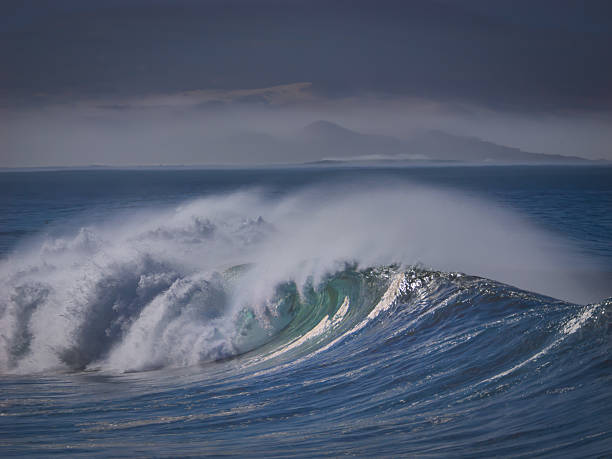 Powerful ocean wave with green curl breaks into turbulent mass of white foam