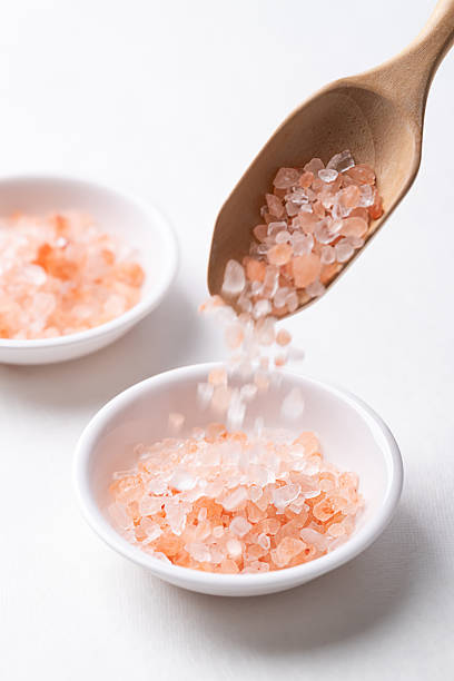 Himalayan pink salt in spoon pouring into bowl on white background