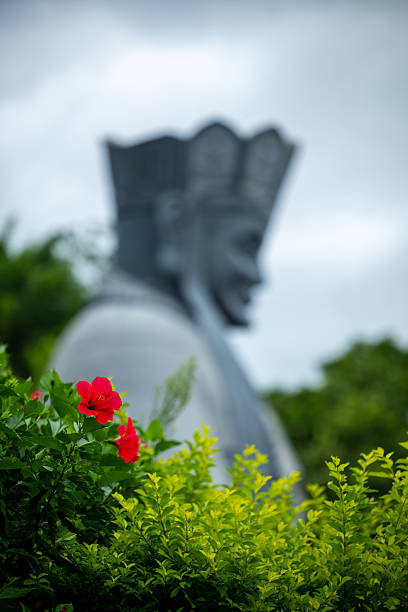 A Statue Surrounded by Flowers and Lush Greenery Under a Cloudy Sky