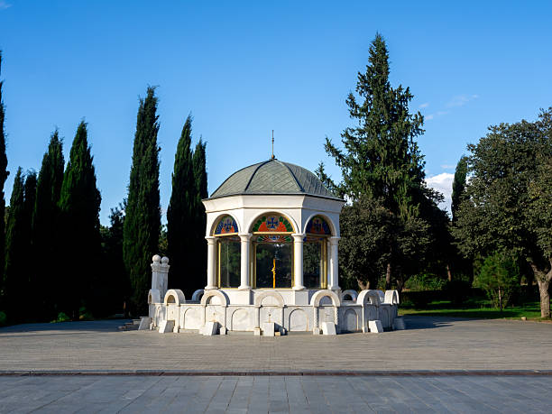 istock Gazebo-style pavilion inside the Holy Trinity Cathedral grounds in Tbilisi, Georgia, featuring stained glass windows, white columns, and peaceful surroundings with evergreen trees under blue sky. 2237969207
