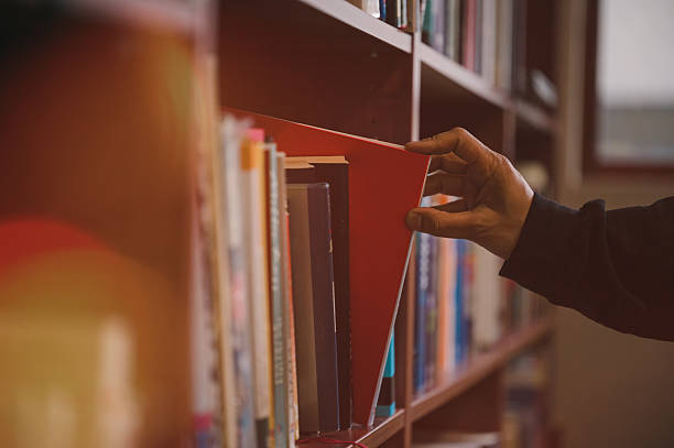istock Hand picking book from library bookshelf for reading and education concept, symbolizing knowledge, education, learning, research, study, literature, academic resources in a quiet study environment 2237970385