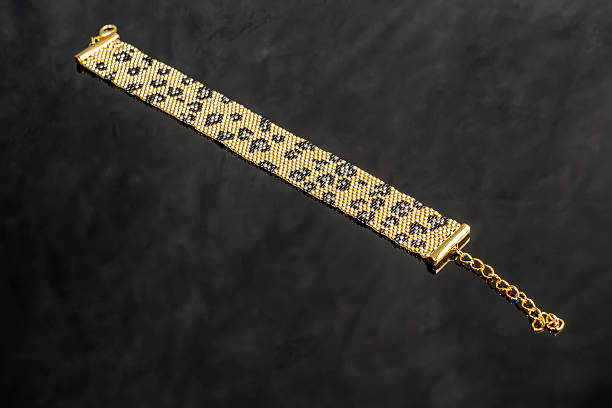 A gold bracelet with a leopard print made of handmade Japanese beads on a light background. Jewelry.