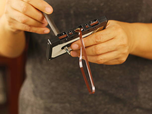 This image depicts a person attempting to repair or manipulate the magnetic tape within an audio cassette using a pencil or similar thin object.