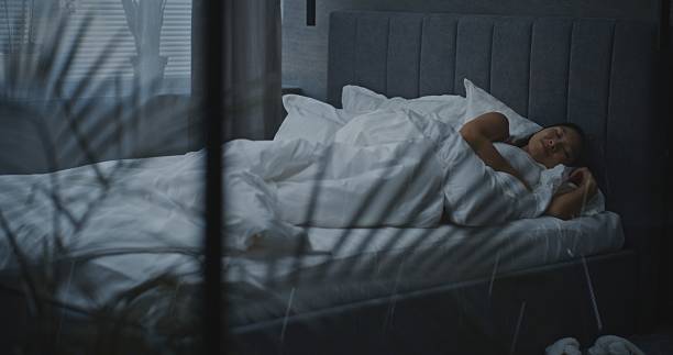 istock Young Woman Lies Down on White Bed and Snuggles Under Soft Blanket 2237990160