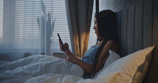 istock Young Woman in Bed Browses Content on Social Media 2237990781