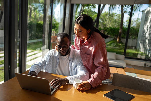 istock Multinational couple enjoying their morning routine, smiling and using laptop and tablet at home 2237995661