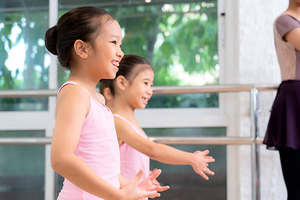 Asian ballet instructor helping girls stretch in ballet studio, flexibility and skill development, healthy lifestyle, children practicing ballet with teacher support, guidance from female dancer.