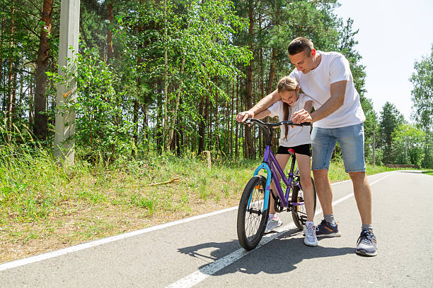 istock Father teaching his daughter how to ride a bicycle in forest 2237998954