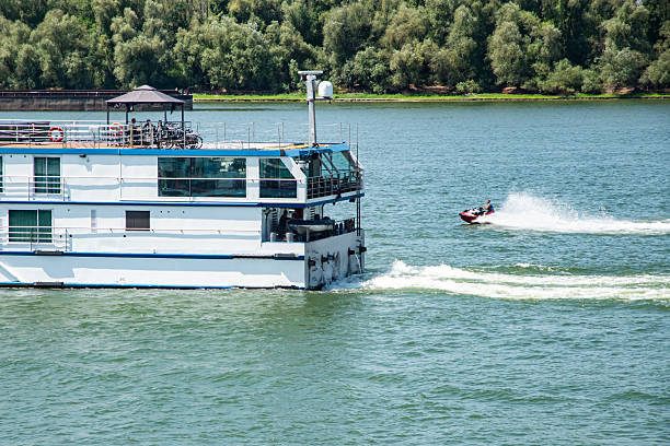 The stern of a river passenger ship and jet ski cutting through the water, leaving foamy wake behind it