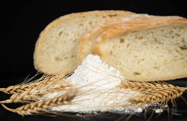 Freshly baked bread with flour and wheat spikes on a dark background showcasing a rustic kitchen setting