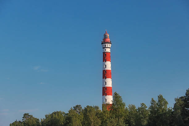 Old lighthouse on background of blue sky and trees on sunny day