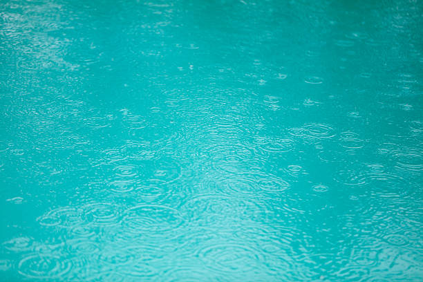 A body of water with raindrops falling on it. The water appears to be a deep blue color, and the raindrops are scattered throughout the scene