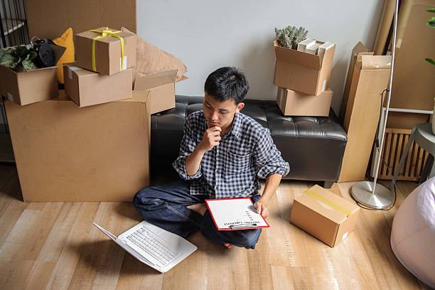 istock Thoughtful Asian Man Looking at Moving Checklist While Using Laptop at New Apartment 2238007381