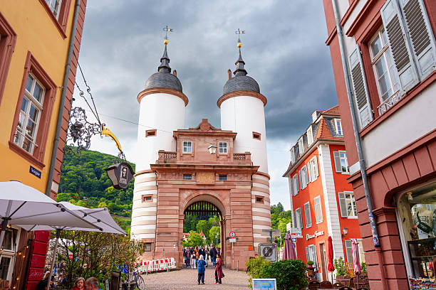 Heidelberg, Germany - June 8, 2025: Archway of the Old Bridge Gate in Heidelberg, Germany, framed by colorful buildings and visitors under an overcast sky.