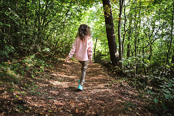 Child walking into a green forest on a dirt path