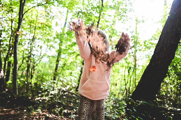 Child enjoying playtime in a forest, throwing leaves and dirt into the air