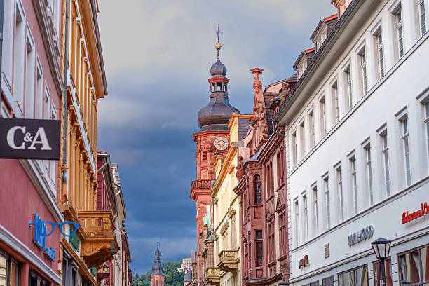 Heidelberg, Germany - June 8, 2025: Charming street view in Heidelberg featuring historic buildings and a prominent clock tower under a dramatic sky.