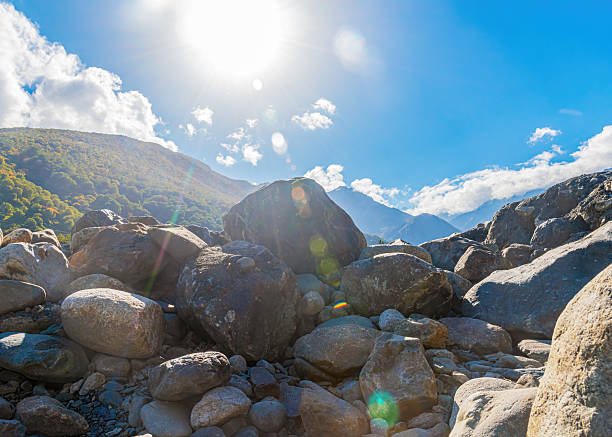large boulder stones against the background of mountains and bright sun with rays with blue sky and clouds