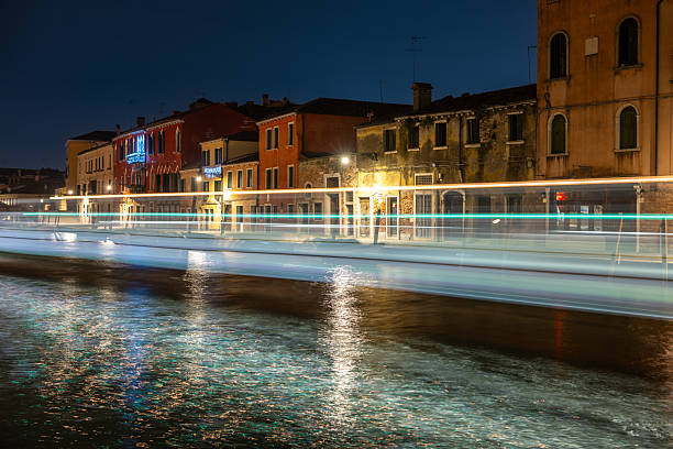 Boats create light trails on Canal Cannaregio as night deepens in Venice, with warm reflections dancing on water and buildings lining the canal.