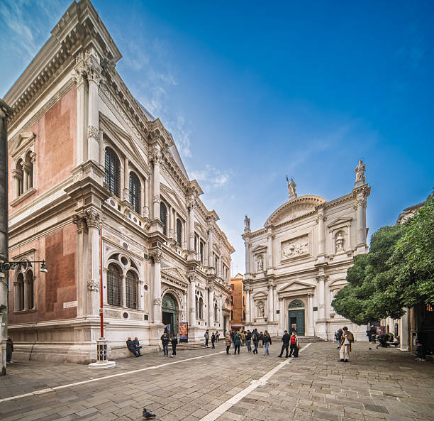Visitors meander through Campo San Rocco, admiring the stunning façades of the Scuola Grande and the Church of San Rocco in Venice's historic heart.