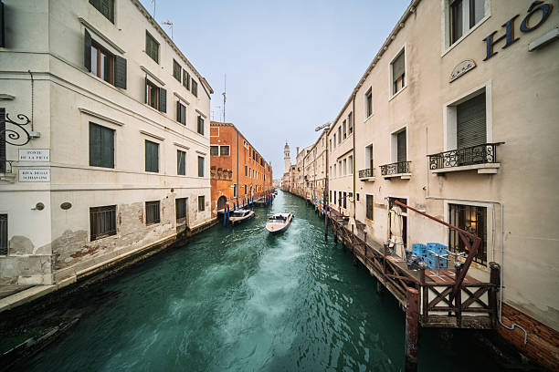 Turquoise waters flow through the narrow Rio dei Greci in Venice, where boats drift past quiet buildings and the campanile watches over the scene.