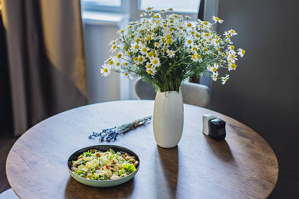 Caesar salad on plate. Bouquet of flowers on table