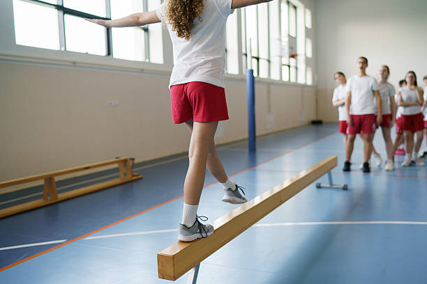 Young girl demonstrating balance and concentration on a gymnastics beam in school gym.