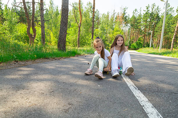 Children riding skateboard in forest at summer.