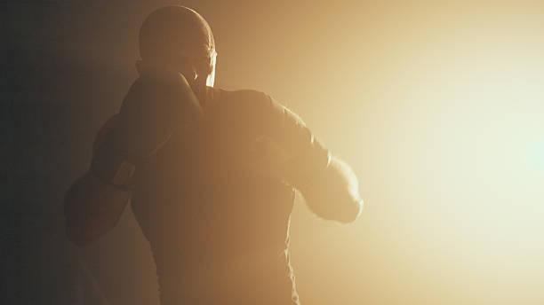 istock Sportsman training for a boxing match alone in a dark room with strong backlight. Practicing punches 2238041457