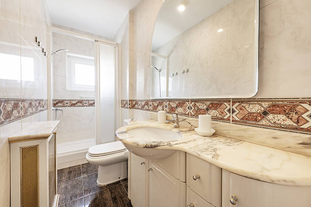 istock Small elongated bathroom with white porcelain sink embedded in veined marble base, frameless mirror, light tile with valances, and white shower stall 2238041567