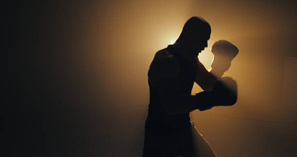 istock Determined sportsman training for a boxing match alone in a dark room with strong backlight. Practicing punching into the air 2238041921