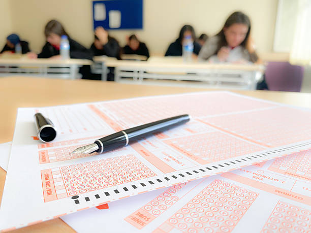 Teenage boys and girls dressed in school uniform concentrating during GCSE examination in hall